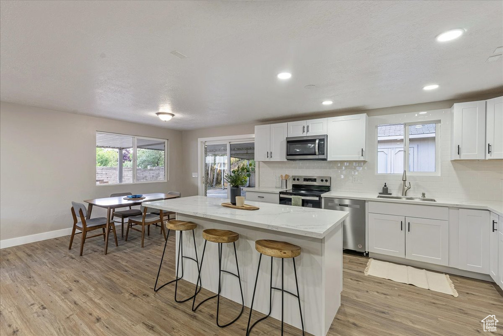 Kitchen with stainless steel appliances, white cabinetry, a center island, light wood-type flooring, and sink