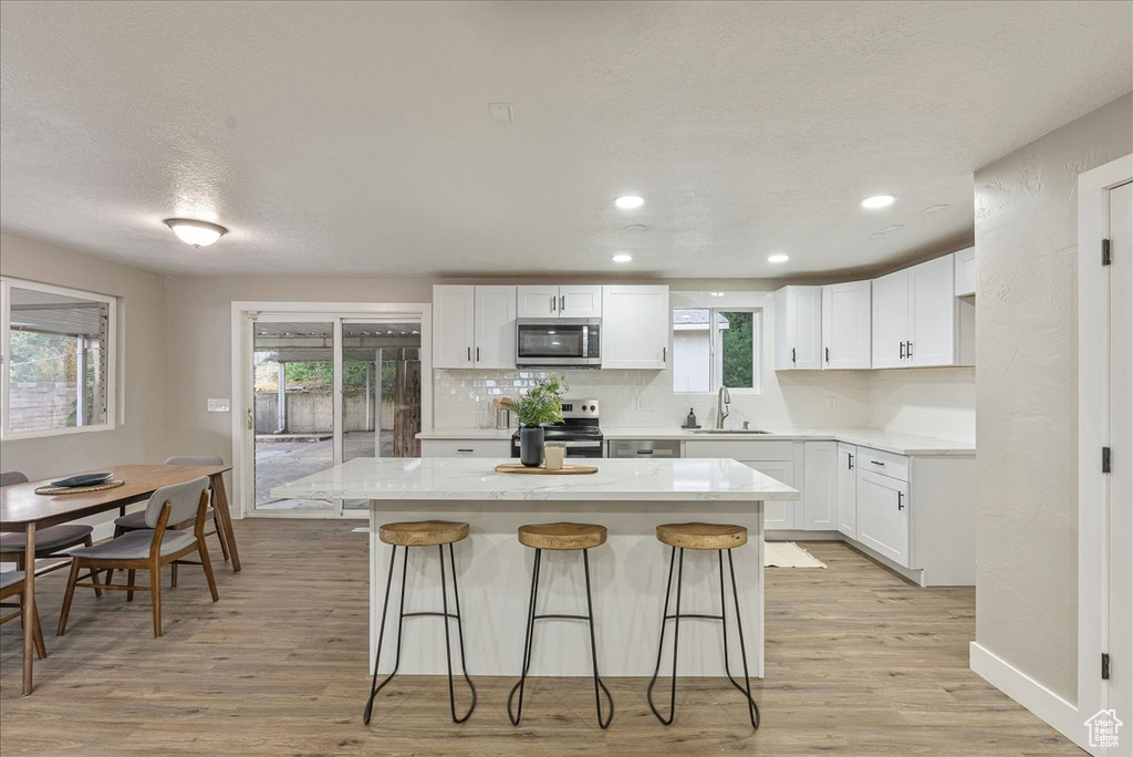 Kitchen with light wood-type flooring, a kitchen island, sink, white cabinetry, and appliances with stainless steel finishes