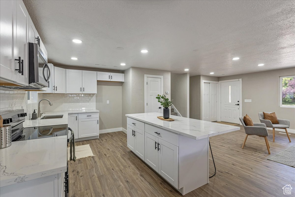 Kitchen with light hardwood / wood-style floors, backsplash, white cabinetry, a center island, and sink