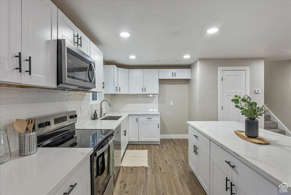 Kitchen with white cabinets, appliances with stainless steel finishes, light hardwood / wood-style flooring, and tasteful backsplash