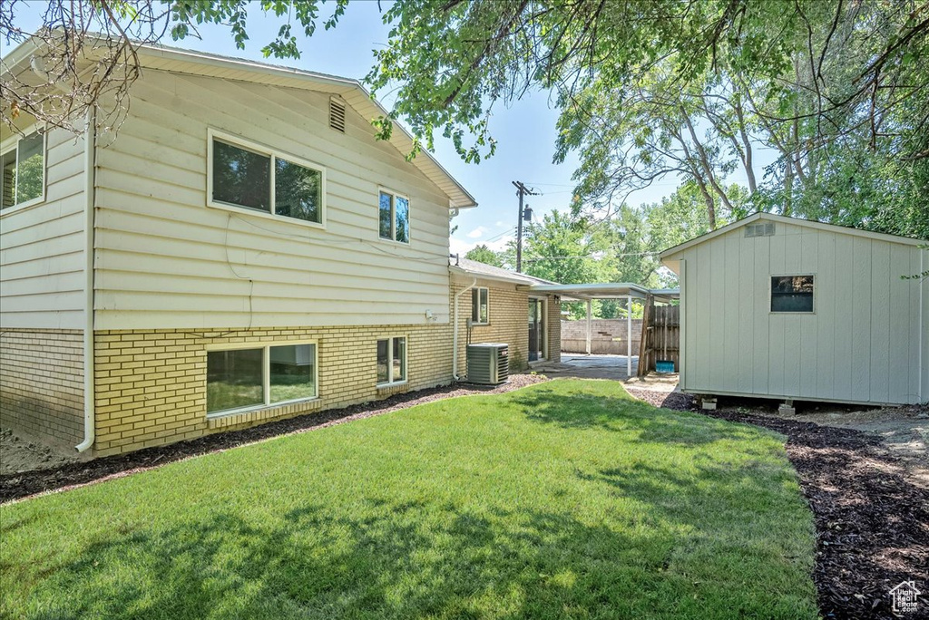 Back of property featuring central AC, a yard, and a storage unit