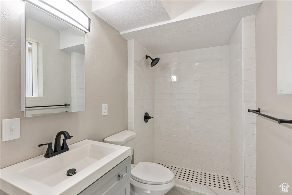 Bathroom with a tile shower, a textured ceiling, toilet, and vanity