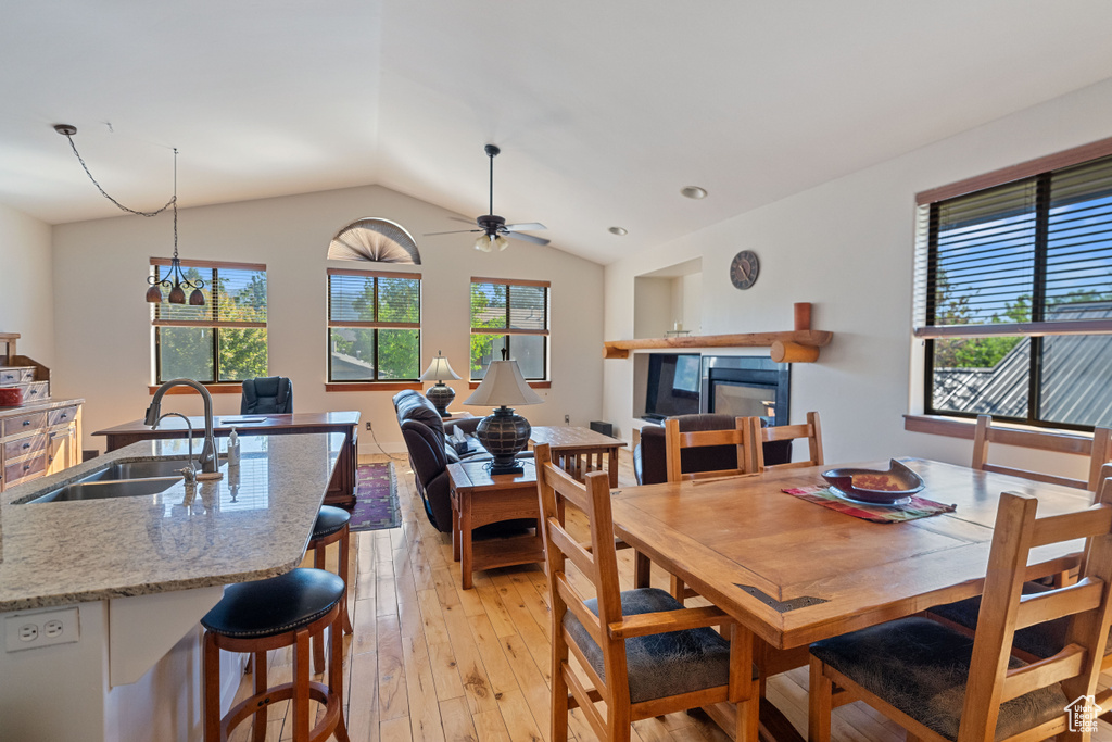 Dining space featuring vaulted ceiling, light hardwood / wood-style floors, ceiling fan with notable chandelier, a tiled fireplace, and sink