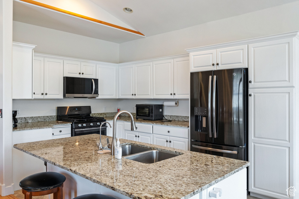 Kitchen with a breakfast bar area, black appliances, lofted ceiling, a kitchen island with sink, and white cabinetry