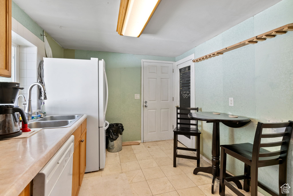 Kitchen featuring sink, white appliances, and light tile floors