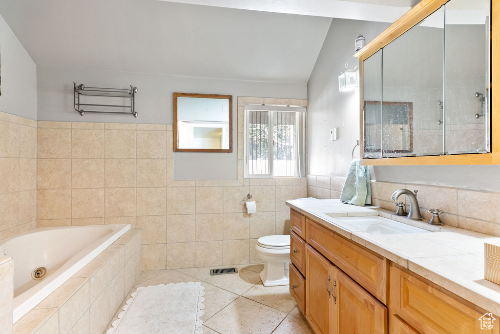 Bathroom featuring vaulted ceiling, vanity with extensive cabinet space, tile walls, tile floors, and toilet