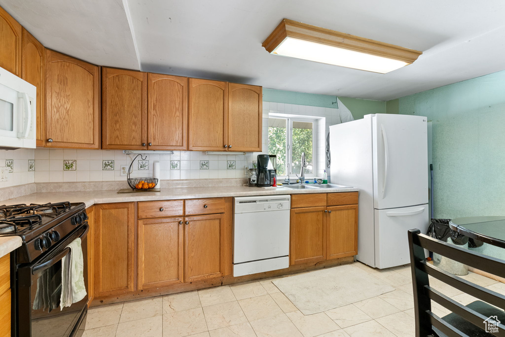 Kitchen featuring white appliances, sink, backsplash, and light tile floors