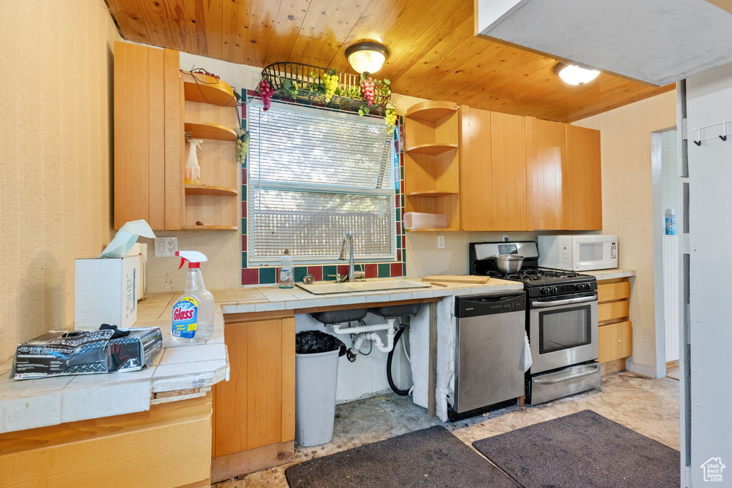 Kitchen with tile counters, stainless steel dishwasher, wooden ceiling, range with gas cooktop, and sink