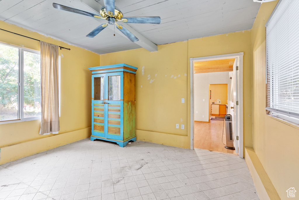 Unfurnished bedroom with ceiling fan, tile flooring, and beamed ceiling