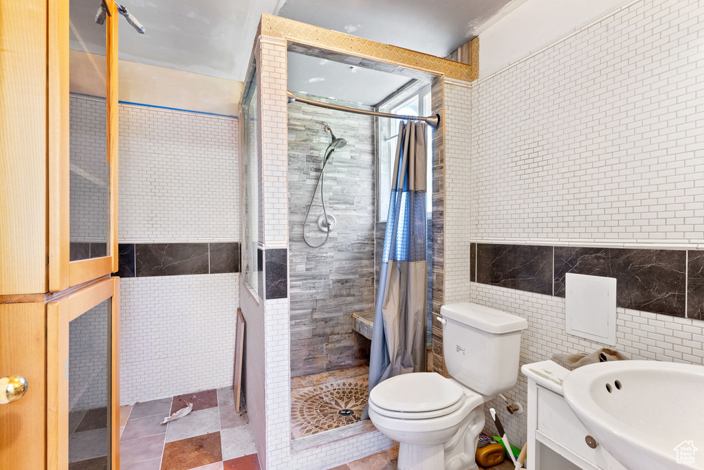 Bathroom with tile walls, tile floors, toilet, and curtained shower