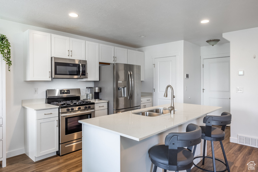 Kitchen featuring stainless steel appliances, a center island with sink, dark wood-type flooring, sink, and white cabinetry