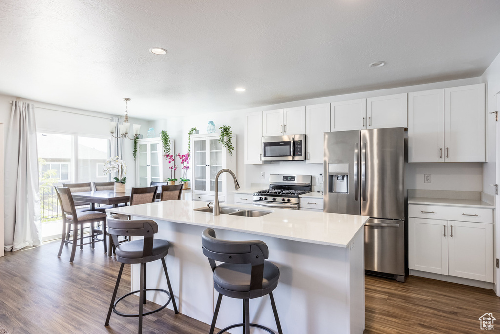 Kitchen featuring appliances with stainless steel finishes, white cabinets, a center island with sink, and dark hardwood / wood-style flooring