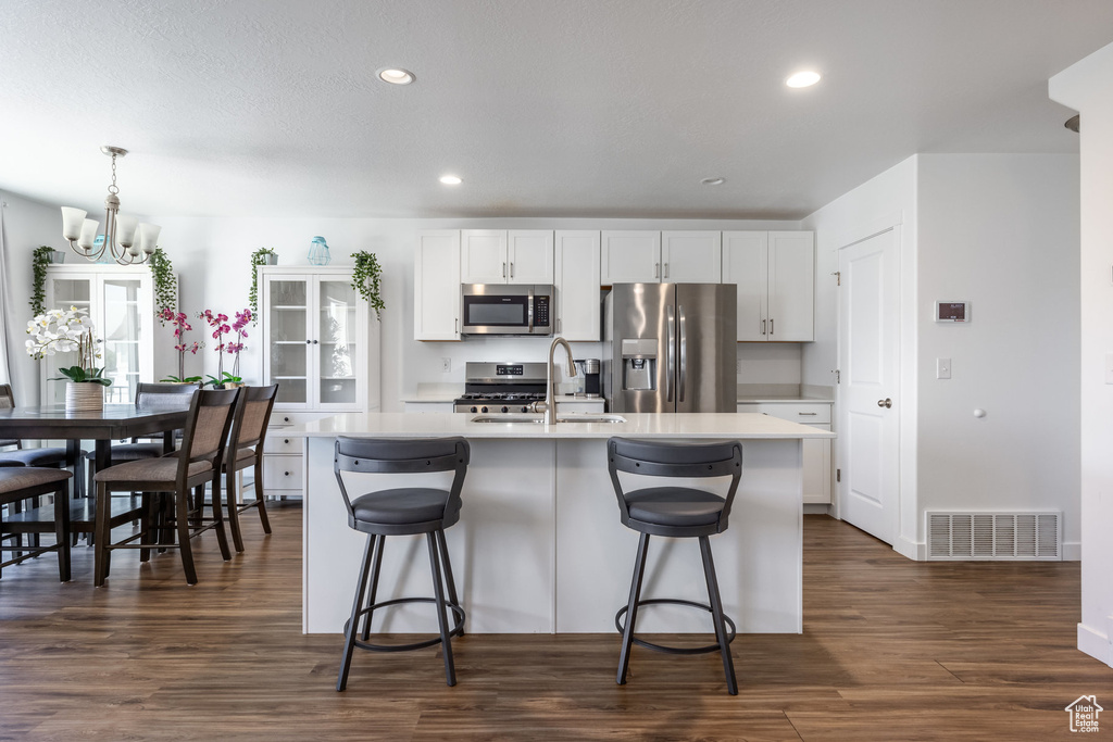 Kitchen featuring stainless steel appliances, white cabinets, a kitchen island with sink, dark hardwood / wood-style floors, and sink