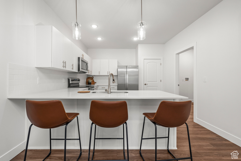 Kitchen featuring decorative light fixtures, tasteful backsplash, dark wood-type flooring, white cabinets, and appliances with stainless steel finishes