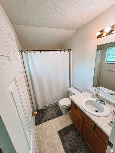 Bathroom featuring tile flooring, a textured ceiling, vaulted ceiling, vanity, and toilet