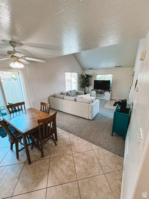 Dining space with ceiling fan, vaulted ceiling, a textured ceiling, and light tile floors