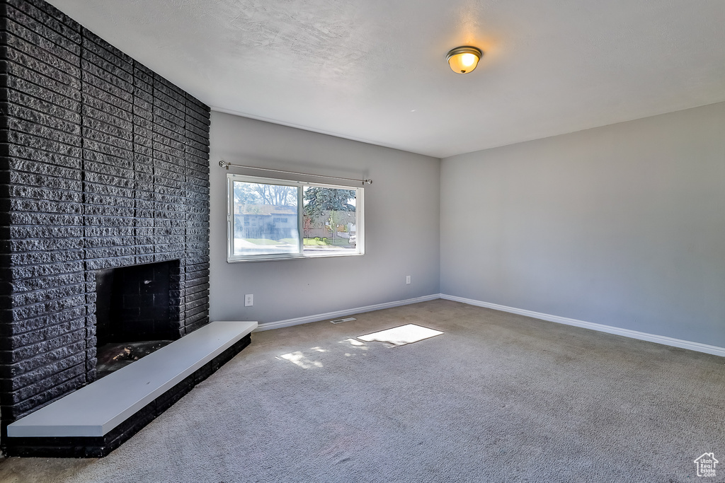 Unfurnished living room with carpet and a brick fireplace