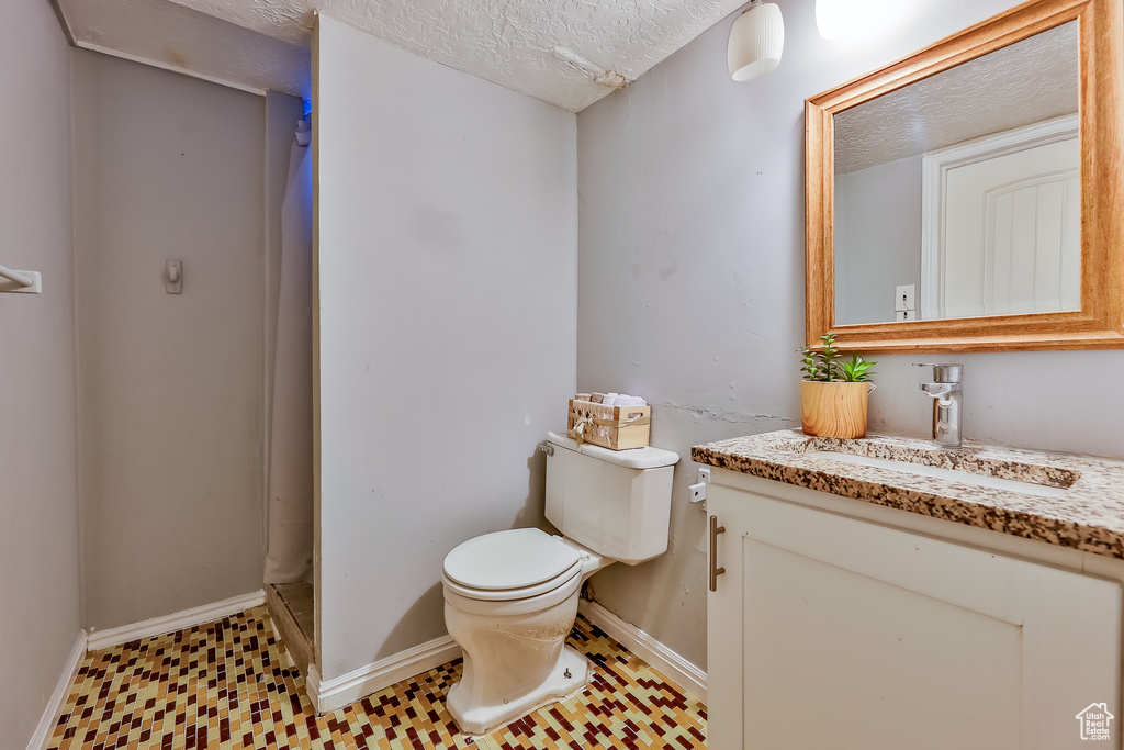 Bathroom with tile patterned flooring, walk in shower, a textured ceiling, toilet, and vanity