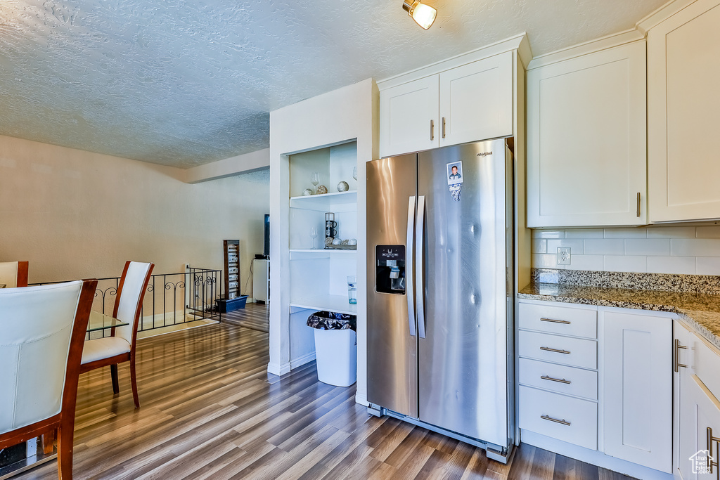 Kitchen featuring stainless steel fridge with ice dispenser, white cabinetry, backsplash, light stone countertops, and hardwood / wood-style flooring