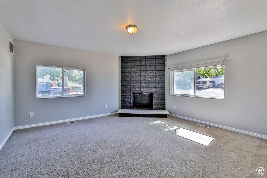 Unfurnished living room featuring brick wall, carpet, and a brick fireplace