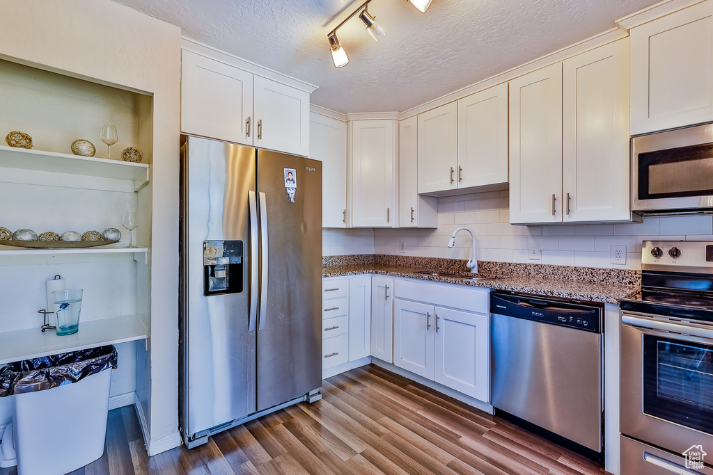 Kitchen with decorative backsplash, rail lighting, sink, appliances with stainless steel finishes, and a textured ceiling