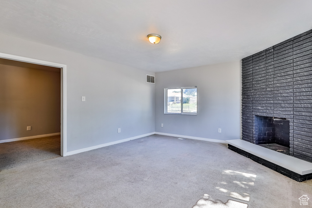 Unfurnished living room featuring a brick fireplace, brick wall, and carpet floors