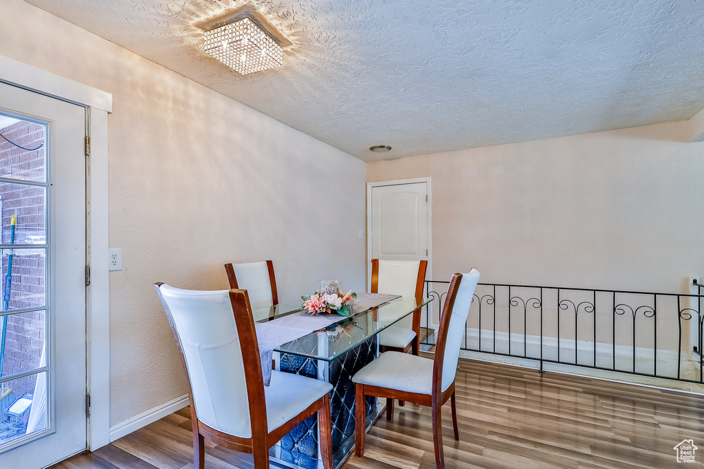 Dining area with a textured ceiling, wood-type flooring, and a notable chandelier