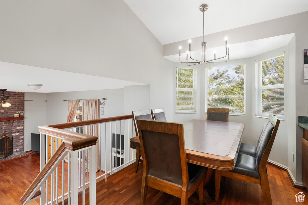 Dining room featuring brick wall, dark hardwood / wood-style flooring, a fireplace, ceiling fan with notable chandelier, and lofted ceiling