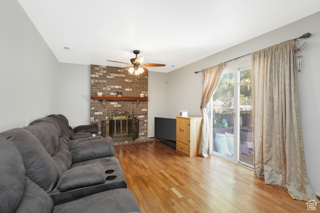 Living room with ceiling fan, light hardwood / wood-style floors, brick wall, and a brick fireplace