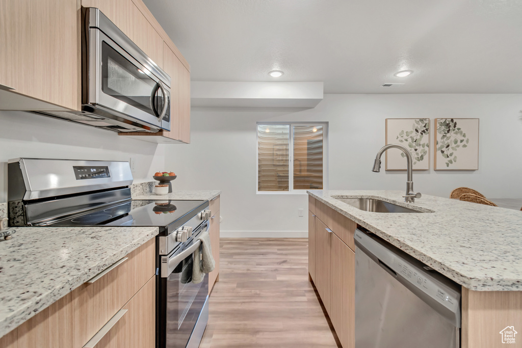 Kitchen with light brown cabinets, light wood-type flooring, stainless steel appliances, sink, and a center island with sink