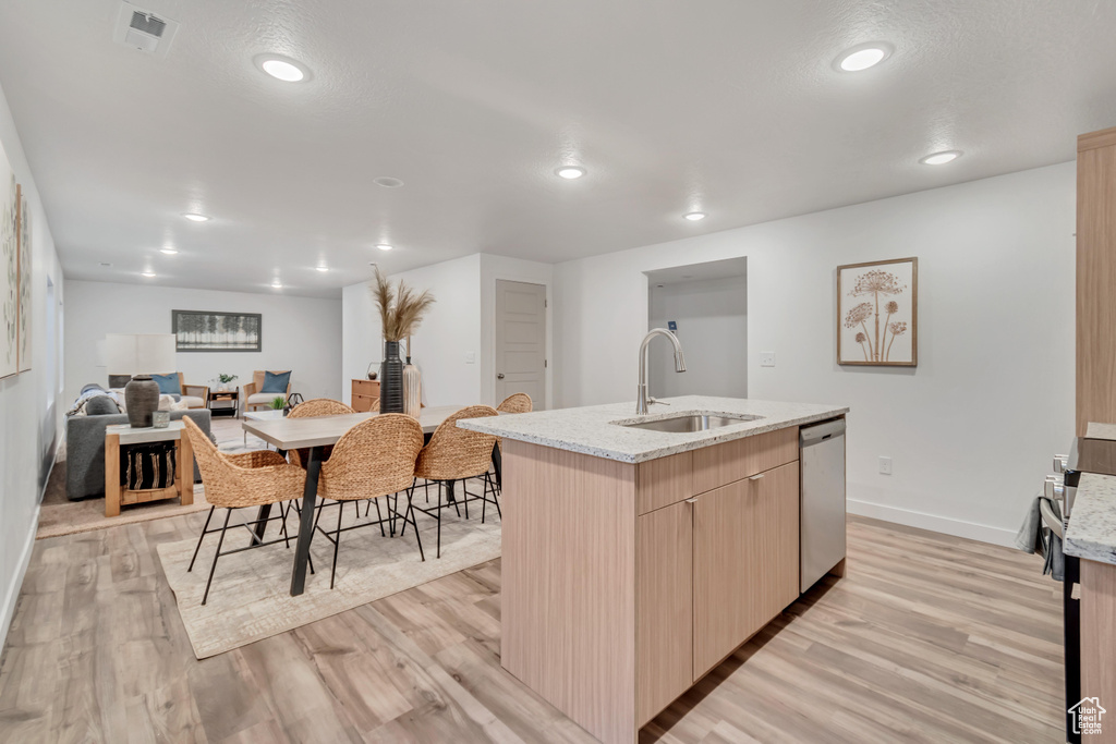 Kitchen featuring light hardwood / wood-style floors, light stone countertops, sink, and an island with sink