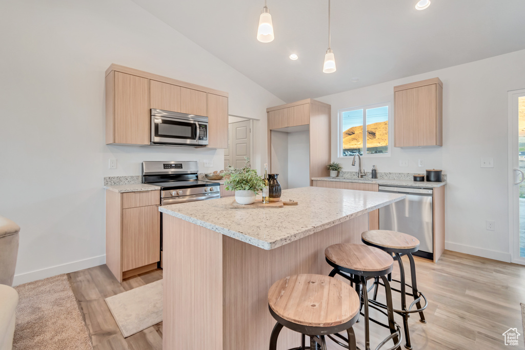 Kitchen with appliances with stainless steel finishes, vaulted ceiling, light wood-type flooring, and a kitchen island