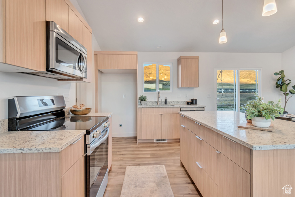 Kitchen with a center island, appliances with stainless steel finishes, light wood-type flooring, and light brown cabinets