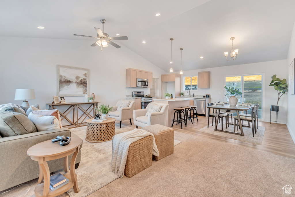 Living room with ceiling fan with notable chandelier, light hardwood / wood-style floors, sink, and high vaulted ceiling