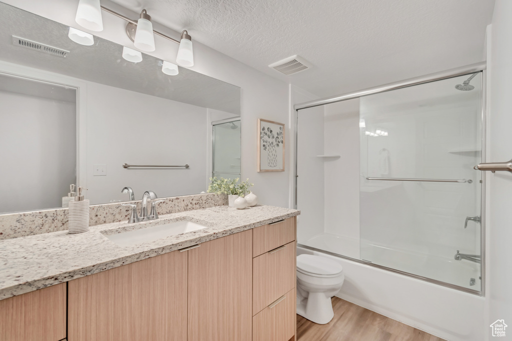 Full bathroom featuring shower / bath combination with glass door, a textured ceiling, toilet, vanity, and hardwood / wood-style flooring