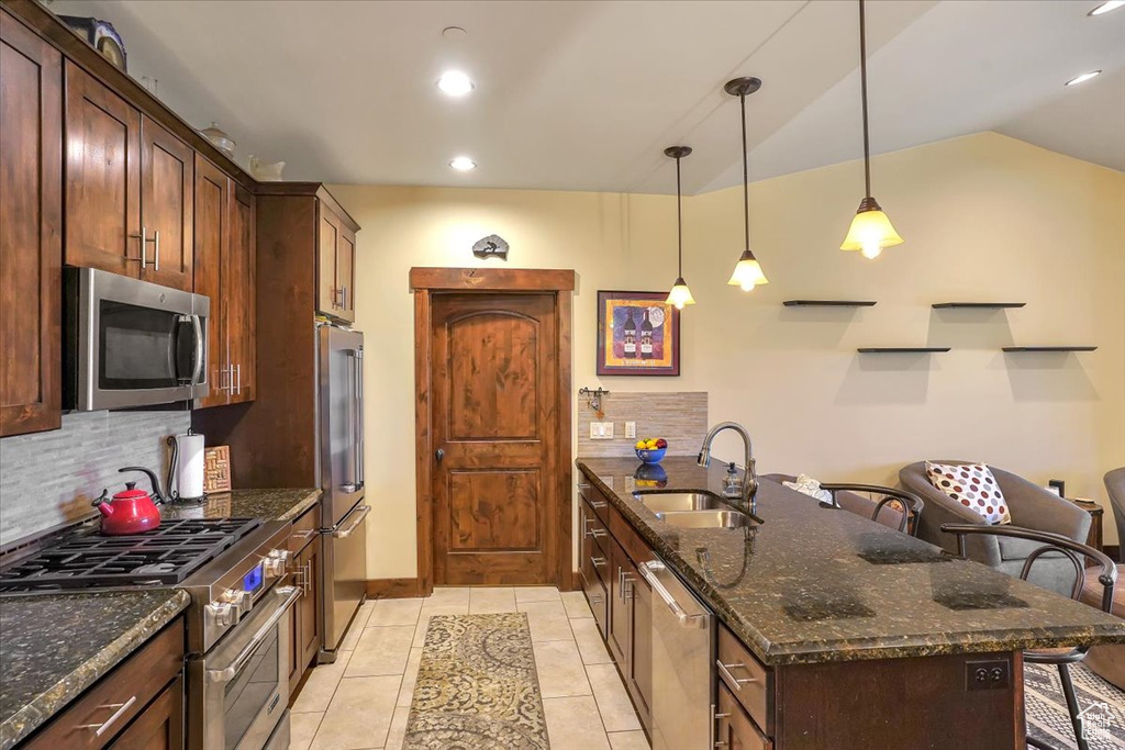 Kitchen with stainless steel appliances, a center island with sink, dark stone countertops, light tile floors, and sink