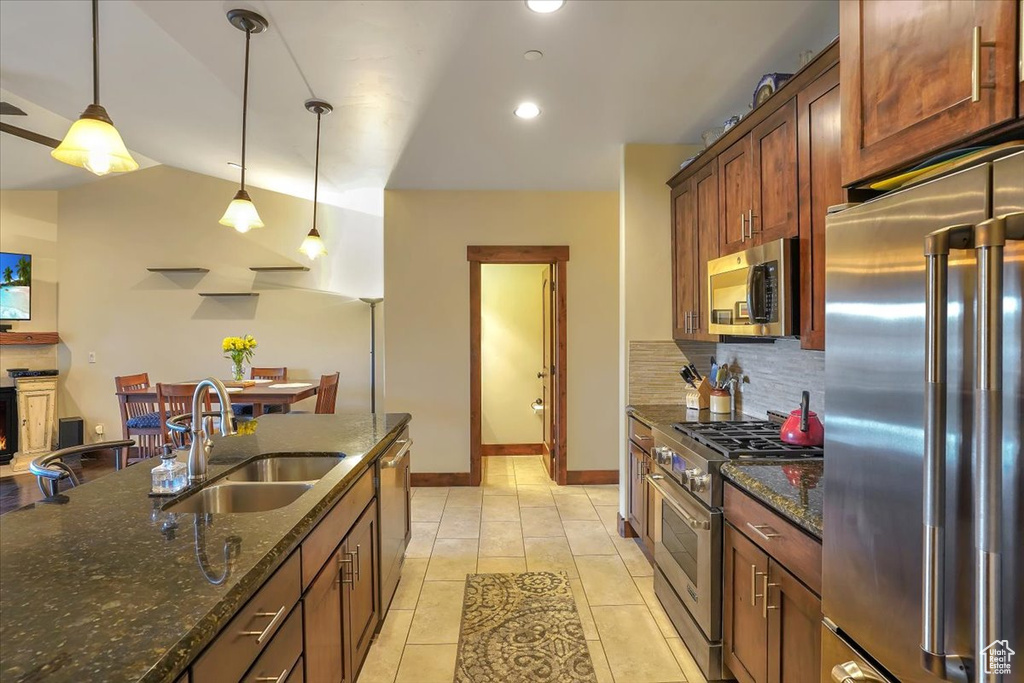 Kitchen featuring dark stone counters, hanging light fixtures, light tile floors, premium appliances, and sink