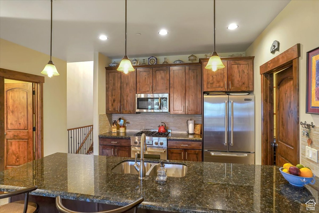 Kitchen featuring dark stone counters, tasteful backsplash, premium appliances, and pendant lighting