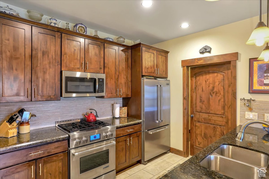 Kitchen with dark stone counters, hanging light fixtures, high end appliances, sink, and light tile floors