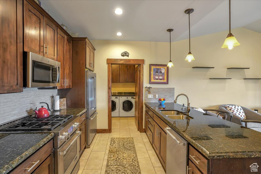 Kitchen featuring stainless steel appliances, washer and dryer, sink, and dark stone countertops