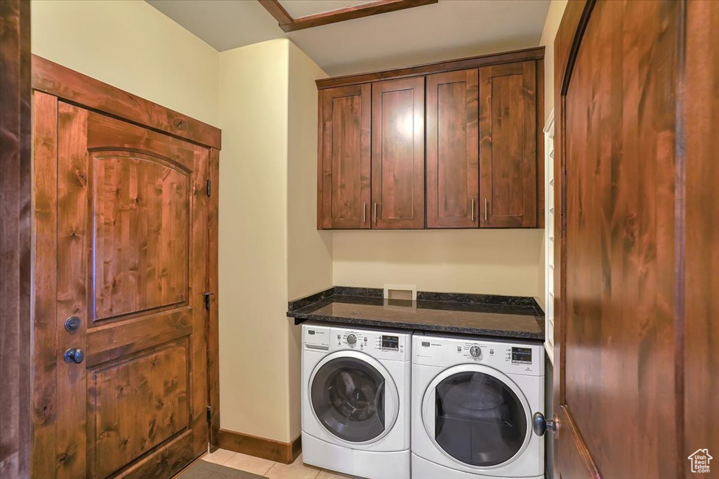 Washroom with cabinets, washer hookup, light tile floors, and washing machine and clothes dryer