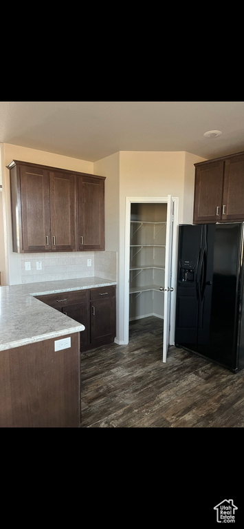 Kitchen featuring black fridge, dark brown cabinets, dark hardwood / wood-style flooring, and backsplash