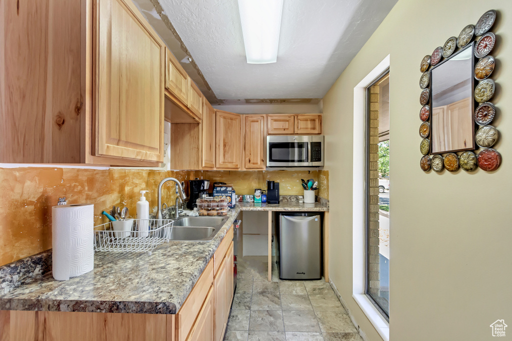 Kitchen featuring light brown cabinetry, light tile flooring, stainless steel appliances, tasteful backsplash, and sink