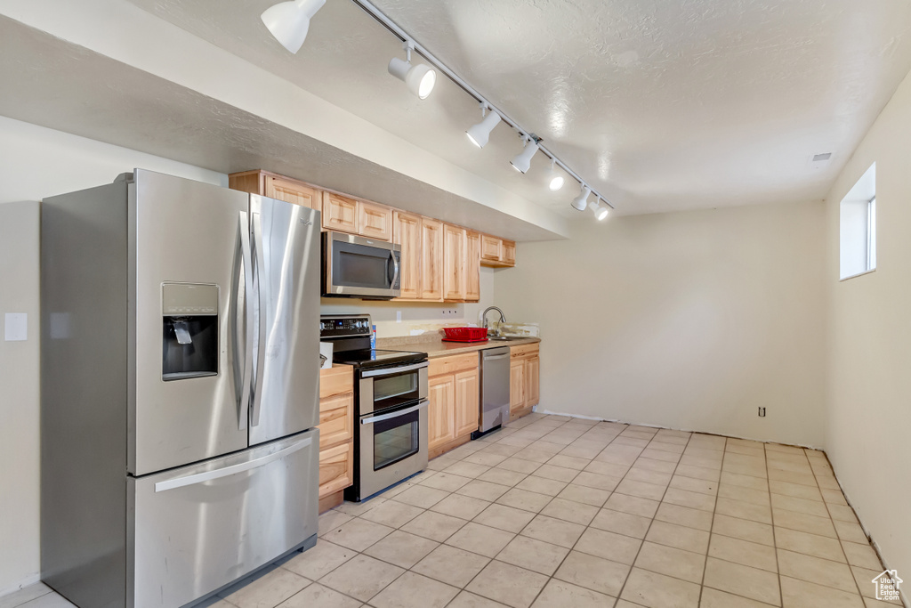 Kitchen featuring light brown cabinetry, track lighting, light tile floors, sink, and appliances with stainless steel finishes