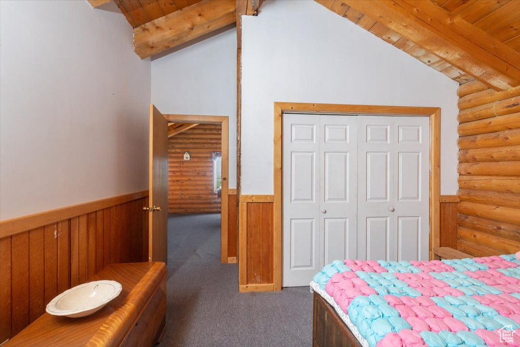 Bedroom with lofted ceiling with beams, a closet, dark carpet, and rustic walls