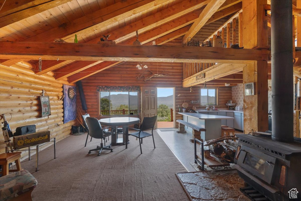 Carpeted dining room featuring a wood stove, beamed ceiling, rustic walls, and wood ceiling