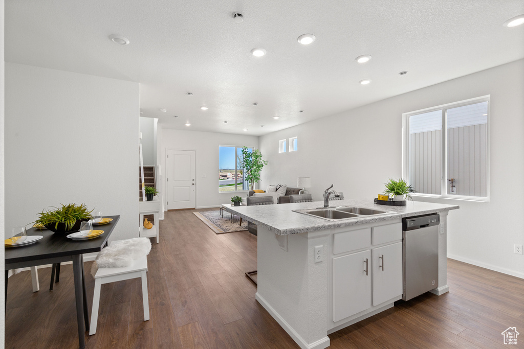 Kitchen with hardwood / wood-style flooring, white cabinets, sink, dishwasher, and a center island with sink