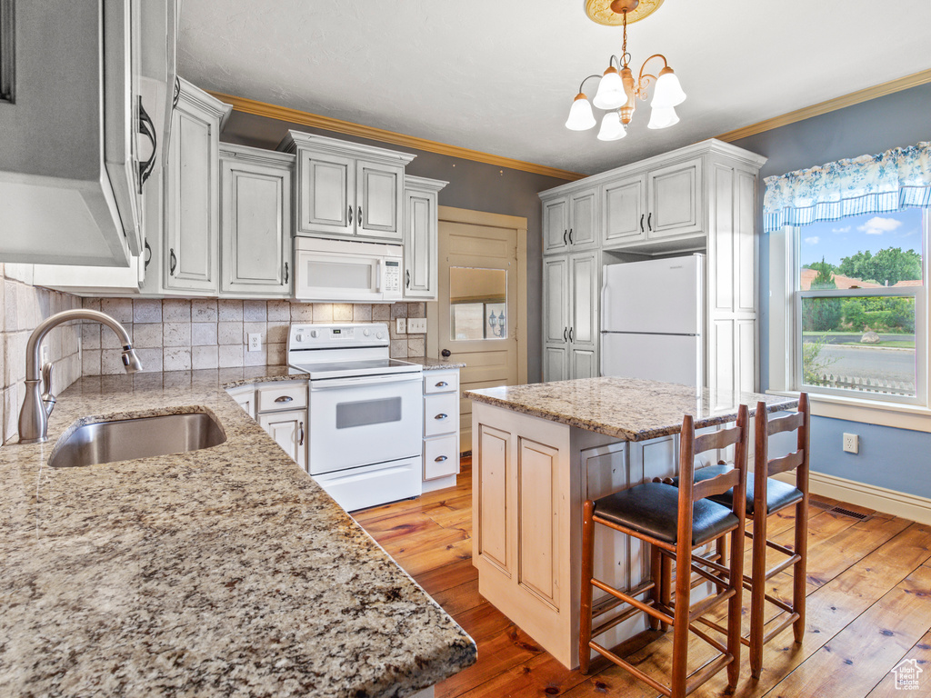 Kitchen featuring hanging light fixtures, tasteful backsplash, light wood-type flooring, sink, and white appliances