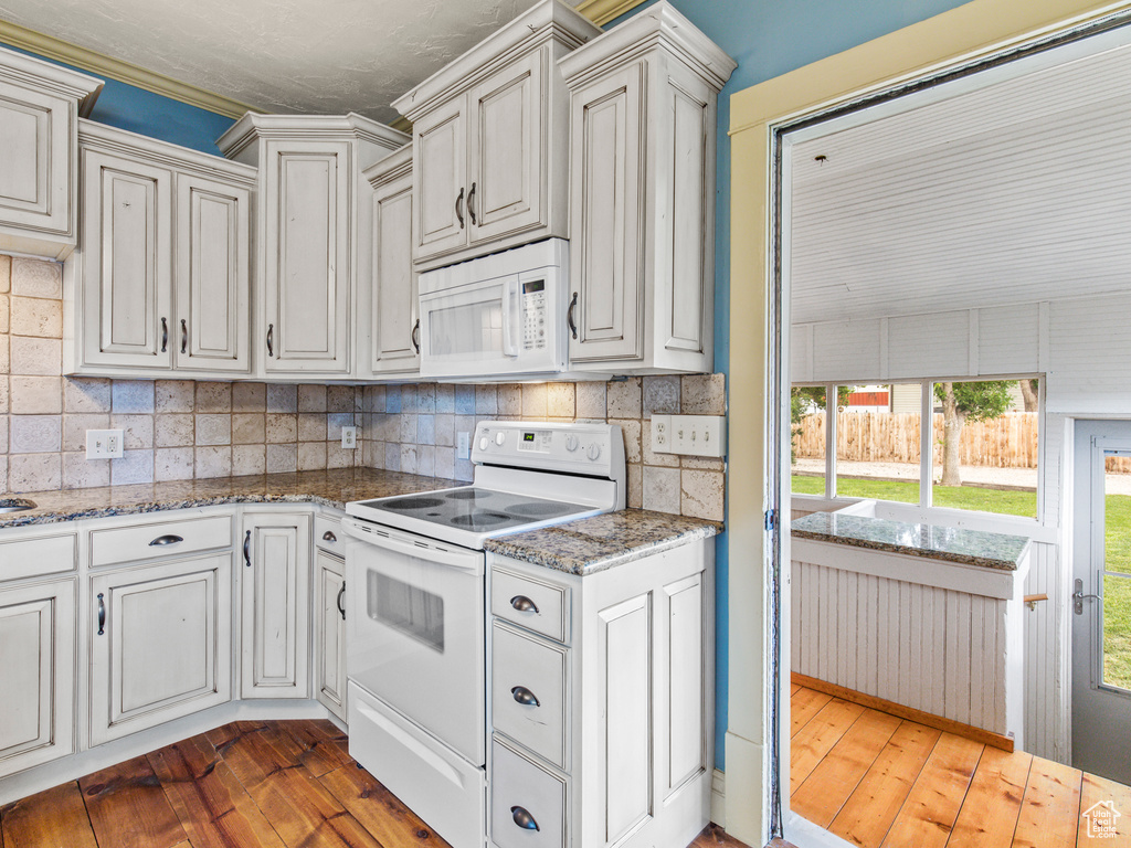 Kitchen with dark wood-type flooring, light stone countertops, white appliances, and tasteful backsplash