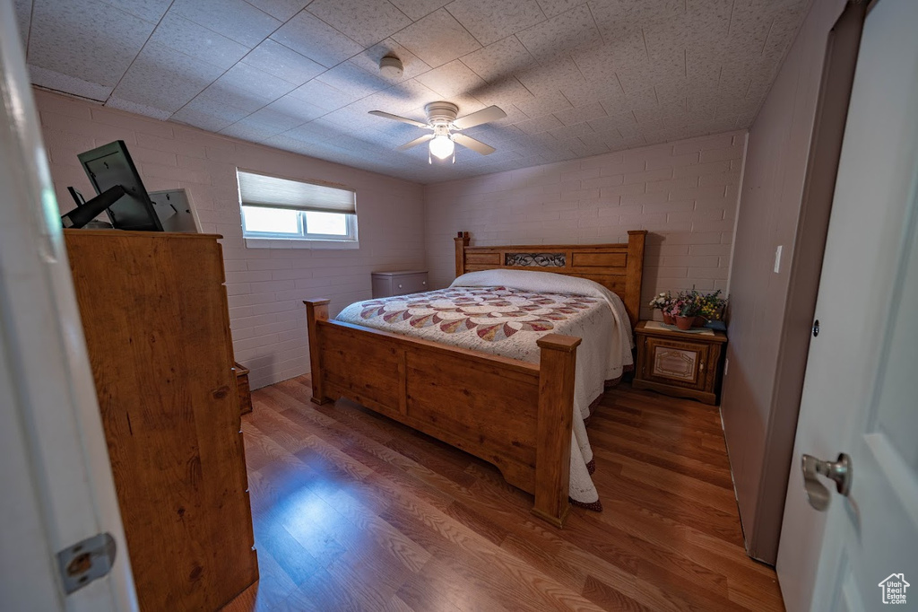 Bedroom with ceiling fan, brick wall, and wood-type flooring